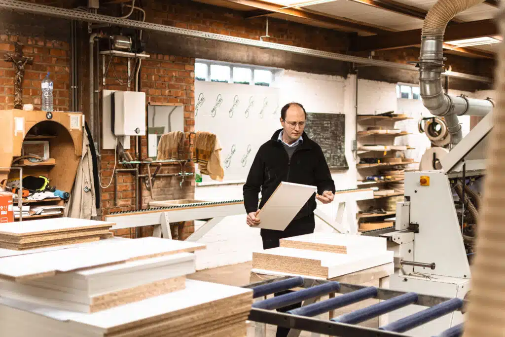 Medewerker van Splendide onderzoekt een wit meubelplaat in het atelier, omringd door houtmateriaal en machines