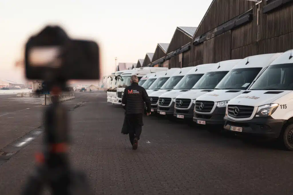 Graviteit-fotograaf filmt Max Mobiel medewerker die voor een rij witte Mercedes-Sprinter bestelwagens loopt bij een magazijn