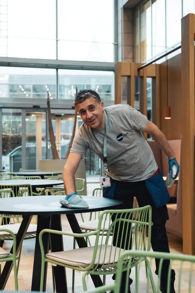 Netto Group medewerker reinigt een tafel in een modern kantoorgebouw in Gent Zuiderpoort met een doek en blauwe handschoenen