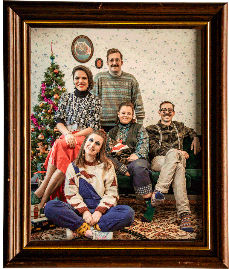 Het Graviteit-team poseert in foute kersttruien als een ouderwets familieportret in een houten kader, naast een versierde kerstboom
