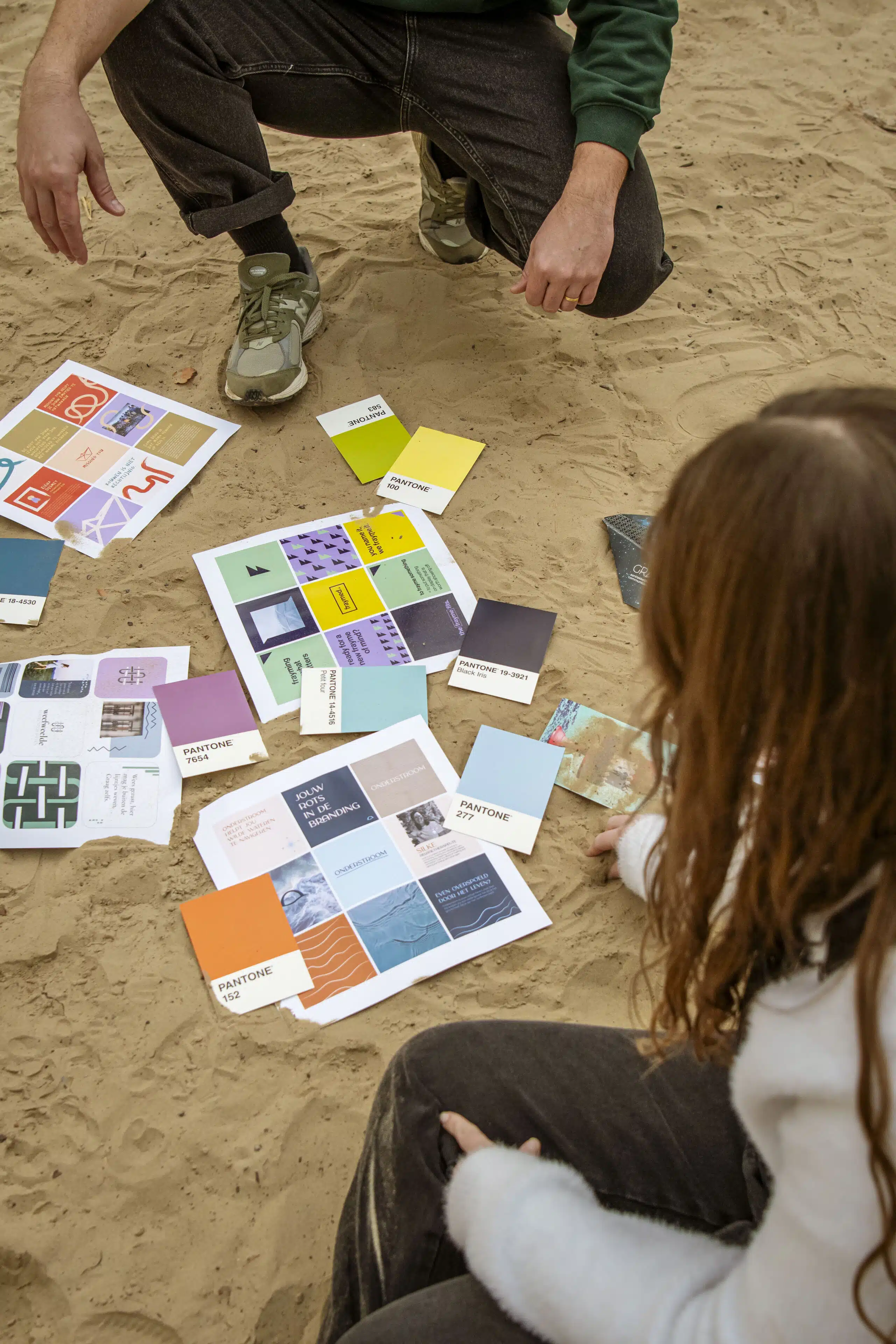 Graviteit-teamleden bekijken Pantone kleurstalen en moodboard prints op het zand tijdens een creatieve branding brainstormses