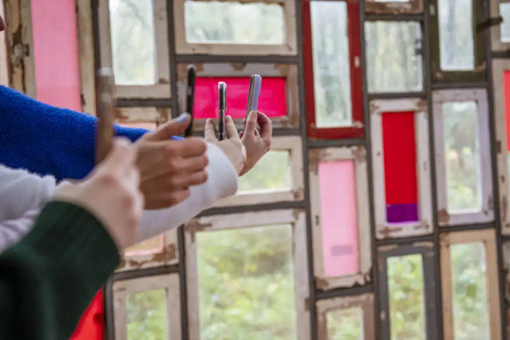 Twee personen fotograferen met smartphones voor een kleurrijke wand van oude raamkozijnen met roze en rode panelen — Gravitei