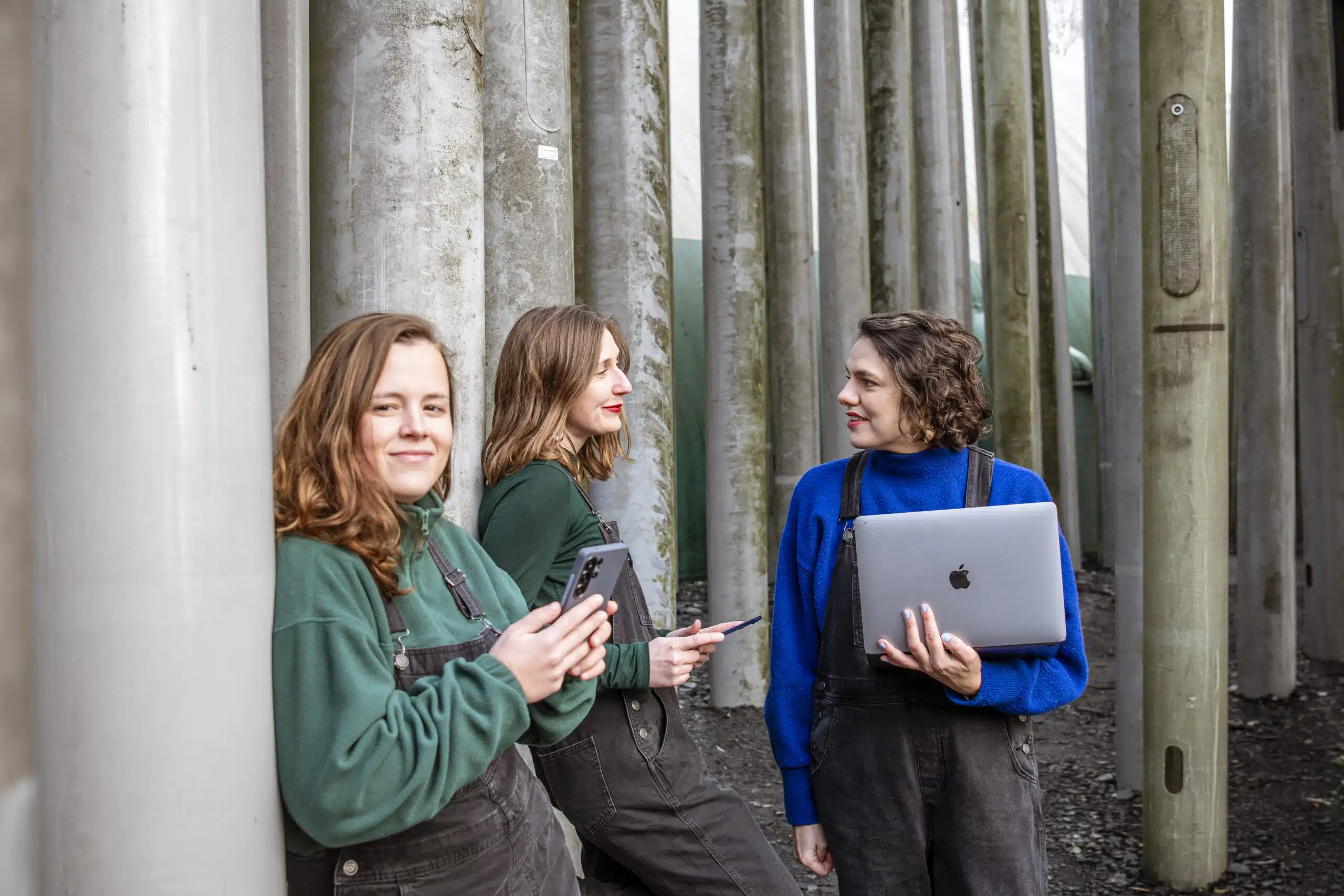Het creatieve team van Graviteit — drie vrouwen met laptop en smartphone — overleggen samen tussen betonnen pilaren