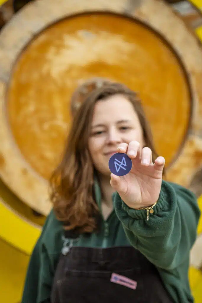 Graviteit-teamlid toont trots het Graviteit-logo op een ronde pin, voor een groot houten vat in Gent