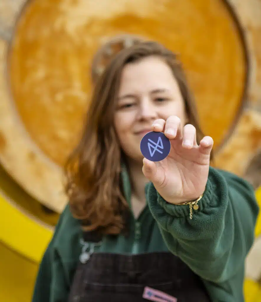 Graviteit-teamlid houdt een rond blauw logo-sticker omhoog voor een houten vat, creatief bureau Graviteit rebranding shoot