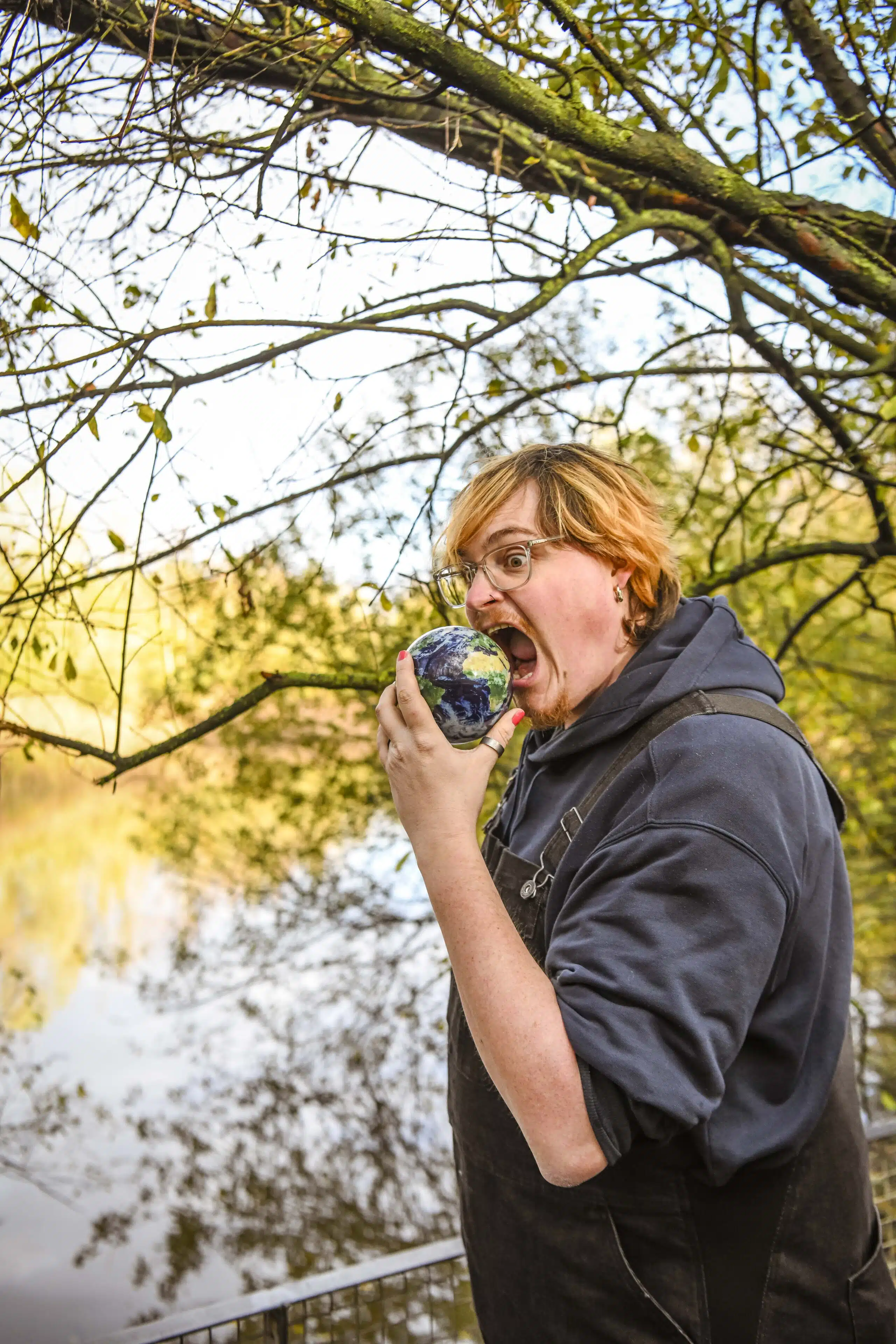 Graviteit-teamlid bijt speels in een kleine wereldbol in de natuur, als creatieve uiting van de rebranding van het communicat