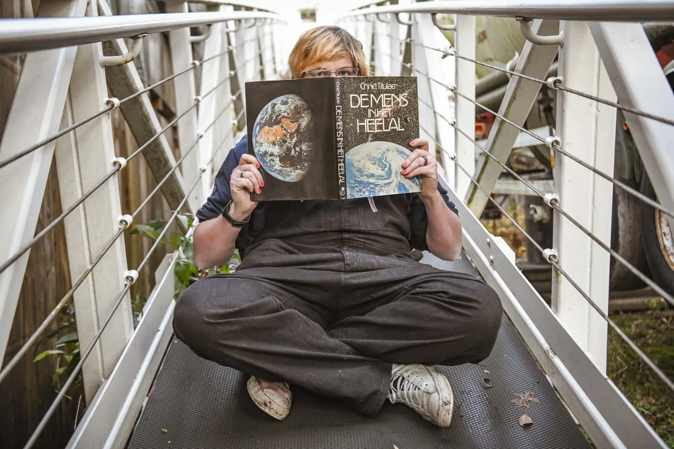 Graviteit teamlid zit gekruisbeend op een loopbrug en houdt het boek 'De Mens in het Heelal' voor haar gezicht