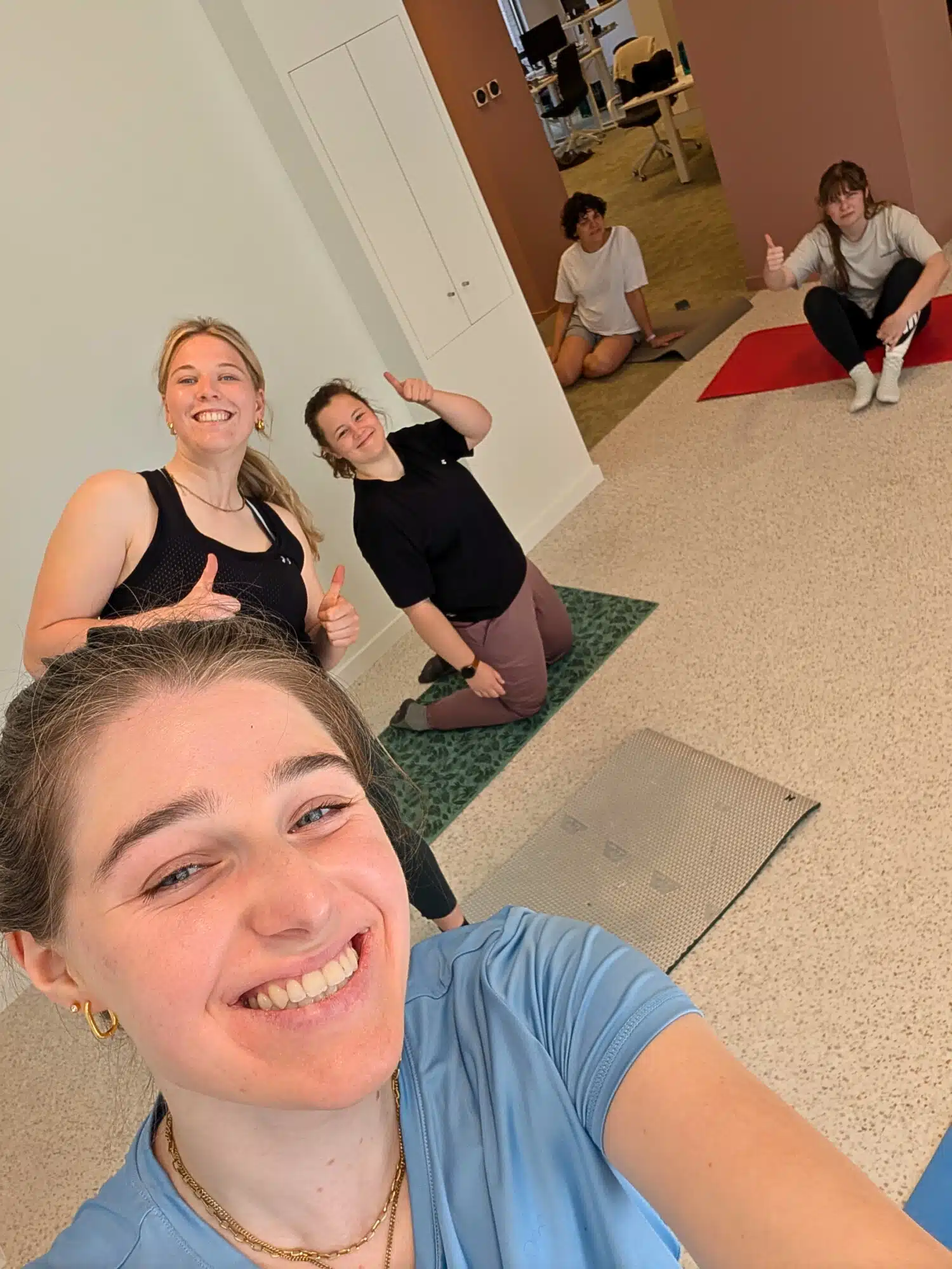 Groep van vijf mensen die samen yoga of pilates beoefenen in een modern kantoor met yogamatten