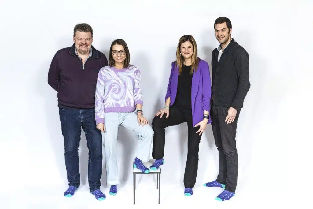 Vier leden van het BeMedico-team poseren samen en tonen hun gecoördineerde kleding. Ze dragen paarse kleding, ze zijn allemaal zelfverzekerd. De casual maar professionele look weerspiegelt de eenheid en benaderbare houding van het team.