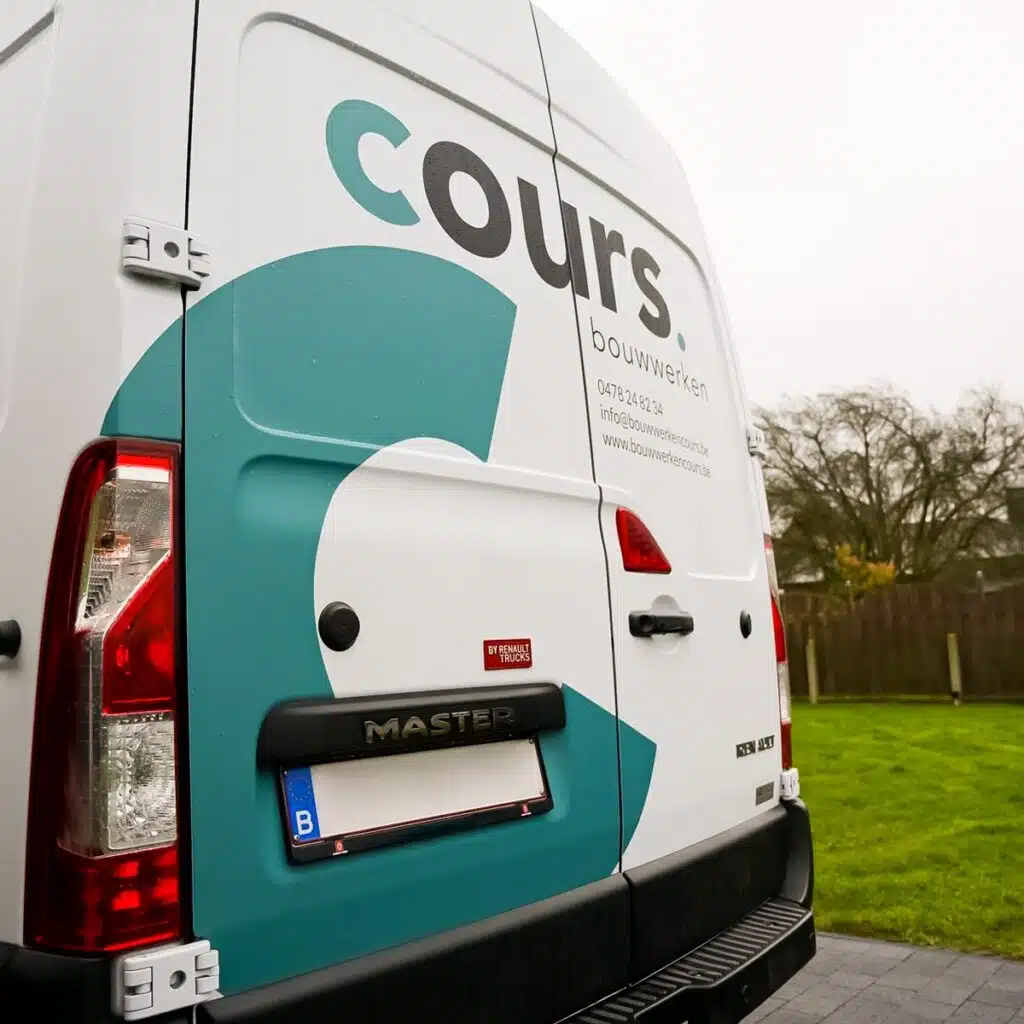 Bestelwagen van Cours - achterkant: Een foto van de achterkant van een witte bestelwagen met het logo en de tekst "cours. bouwwerken" in zwart en groen, geparkeerd op een oprit.