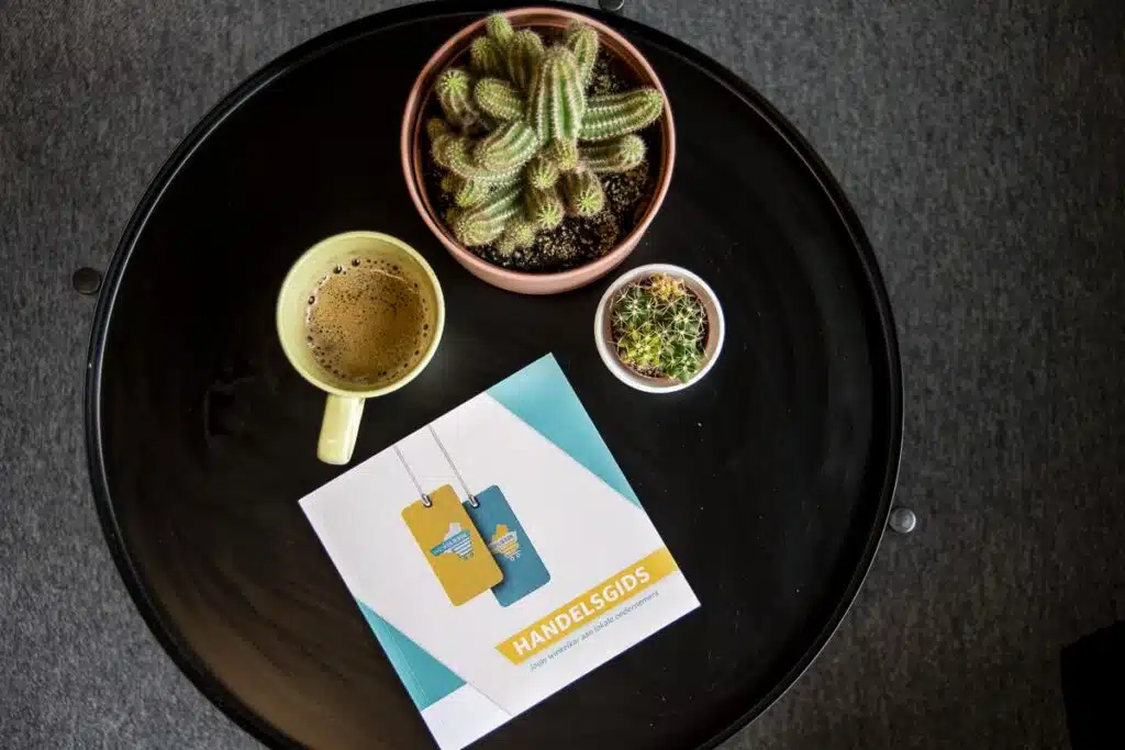 Ronde tafel met koffie en magazine voor Winkelierde: Een ronde zwarte tafel met een kop koffie, een magazine en kleine cactussen.