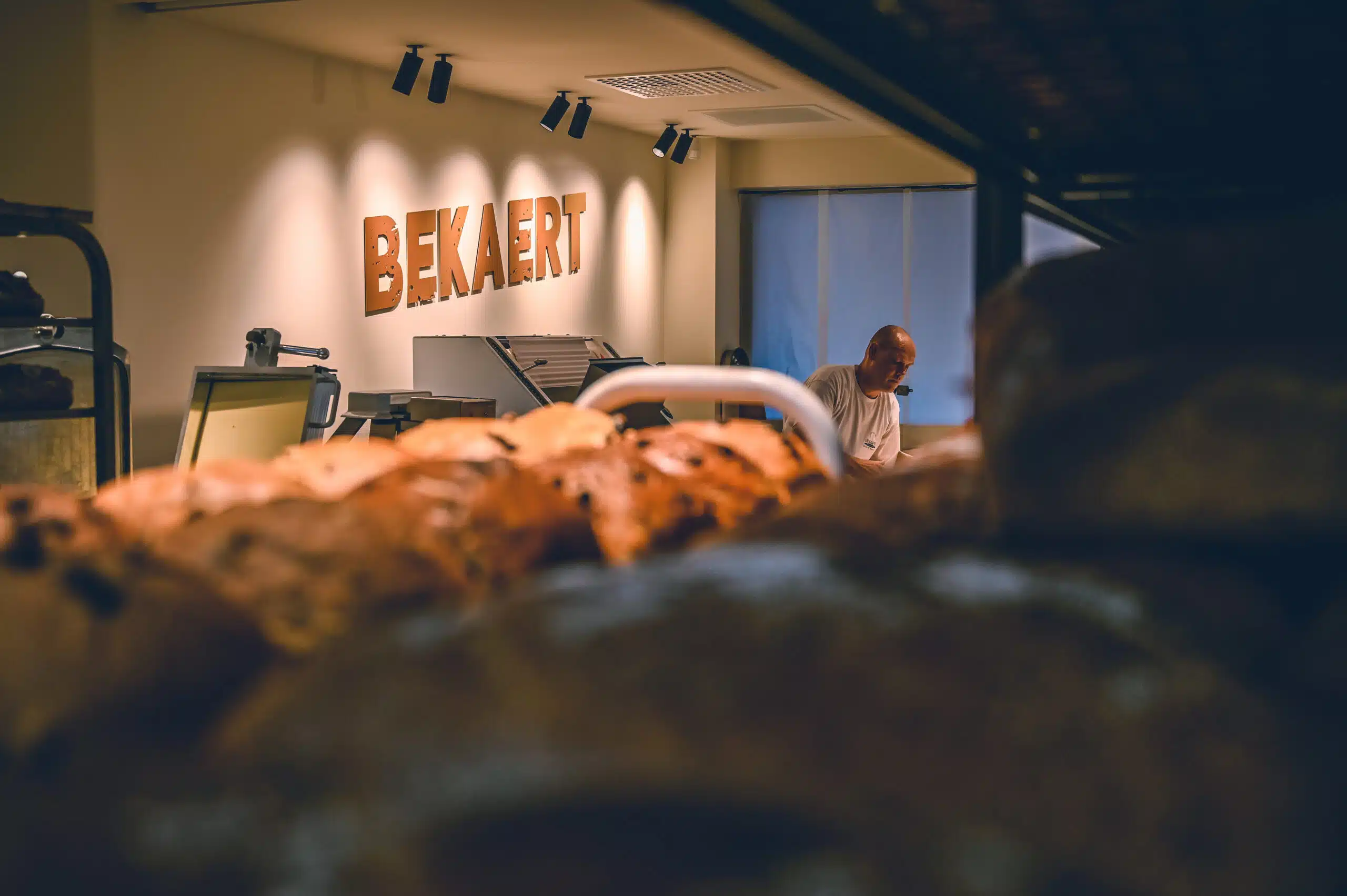 Bakker aan het werk in de ambachtelijke bakkerij Bekaert met vers gebakken brood op de voorgrond.