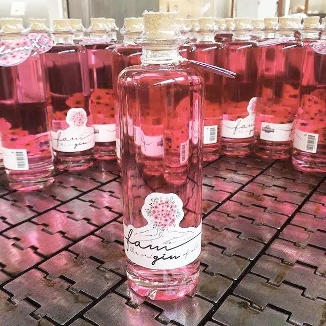 Roze ginflessen met een bloemenetiket en het merk 'Fam' in het midden van een productieband.