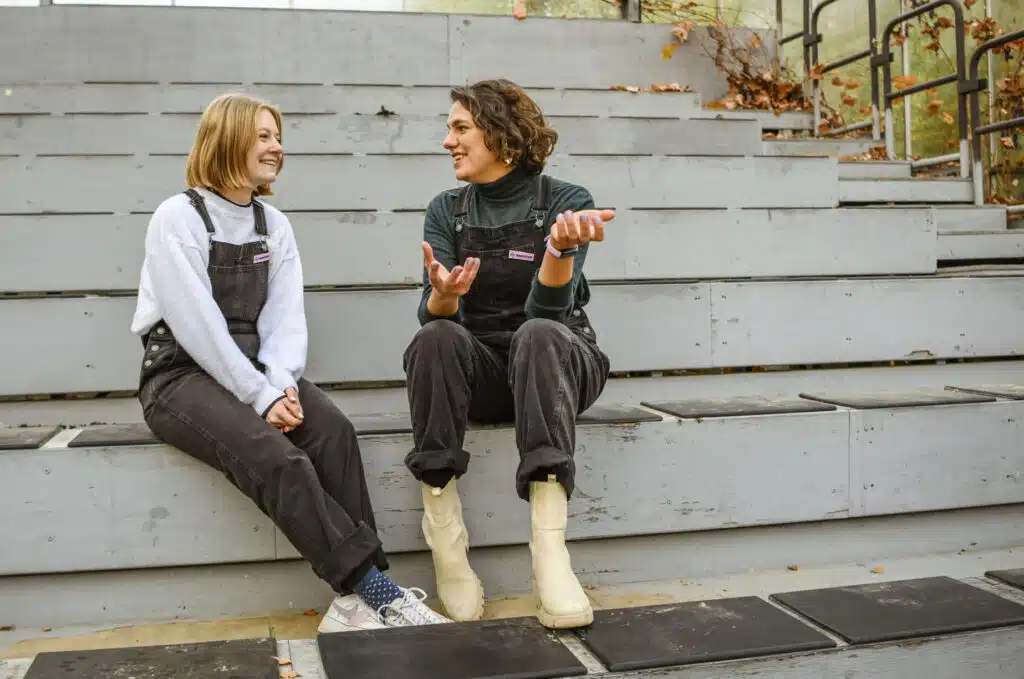 Twee Graviteit-medewerkers in tuinbroek zitten lachend op trappen buiten en bespreken samen een communicatieplan