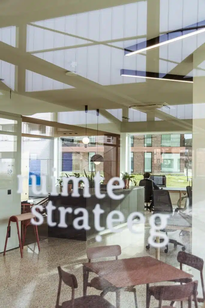 Interieur van het Ruimtestrateeg kantoor gezien door een glazen deur met logo, met een medewerker aan het werk aan een bureau