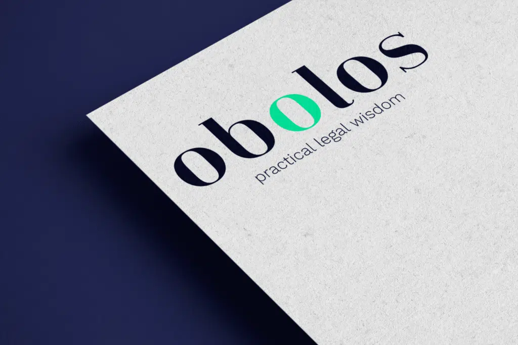 Close-up van een Obolos visitekaartje met logo en motto 'practical legal wisdom' op een getextureerde papieren achtergrond.
