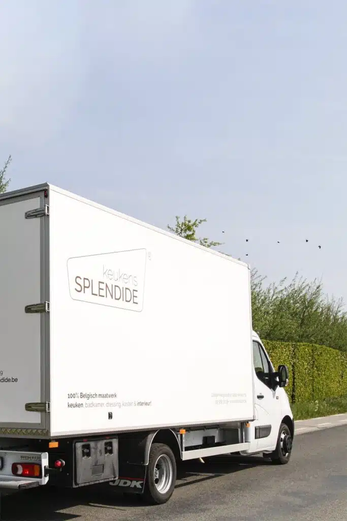 Witte bestelwagen van Keukens Splendide met bedrijfslogo en slogan op een landweg.