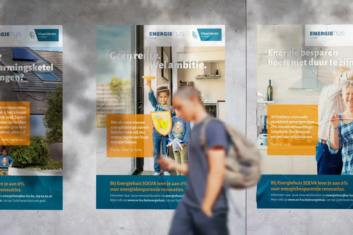 Energiehuis Familieposter voor Solva: Een reeks posters aan een muur, die energiebesparende initiatieven promoten. De posters tonen beelden van gezinnen en individuen met motiverende teksten zoals "Geen rente. Wel ambitie." Het ontwerp gebruikt een mix van blauw en oranje kleuren om warmte en energie-efficiëntie te benadrukken.