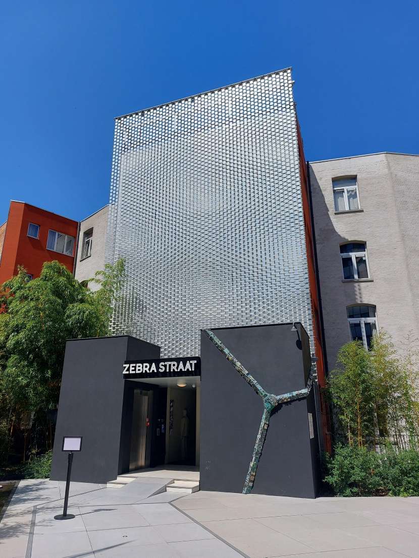 De buitenkant van een gebouw met de naam "Zebra Straat," waarschijnlijk de locatie waar de eerdere afbeeldingen zijn genomen. Het gebouw heeft een moderne gevel met een creatief designelement.