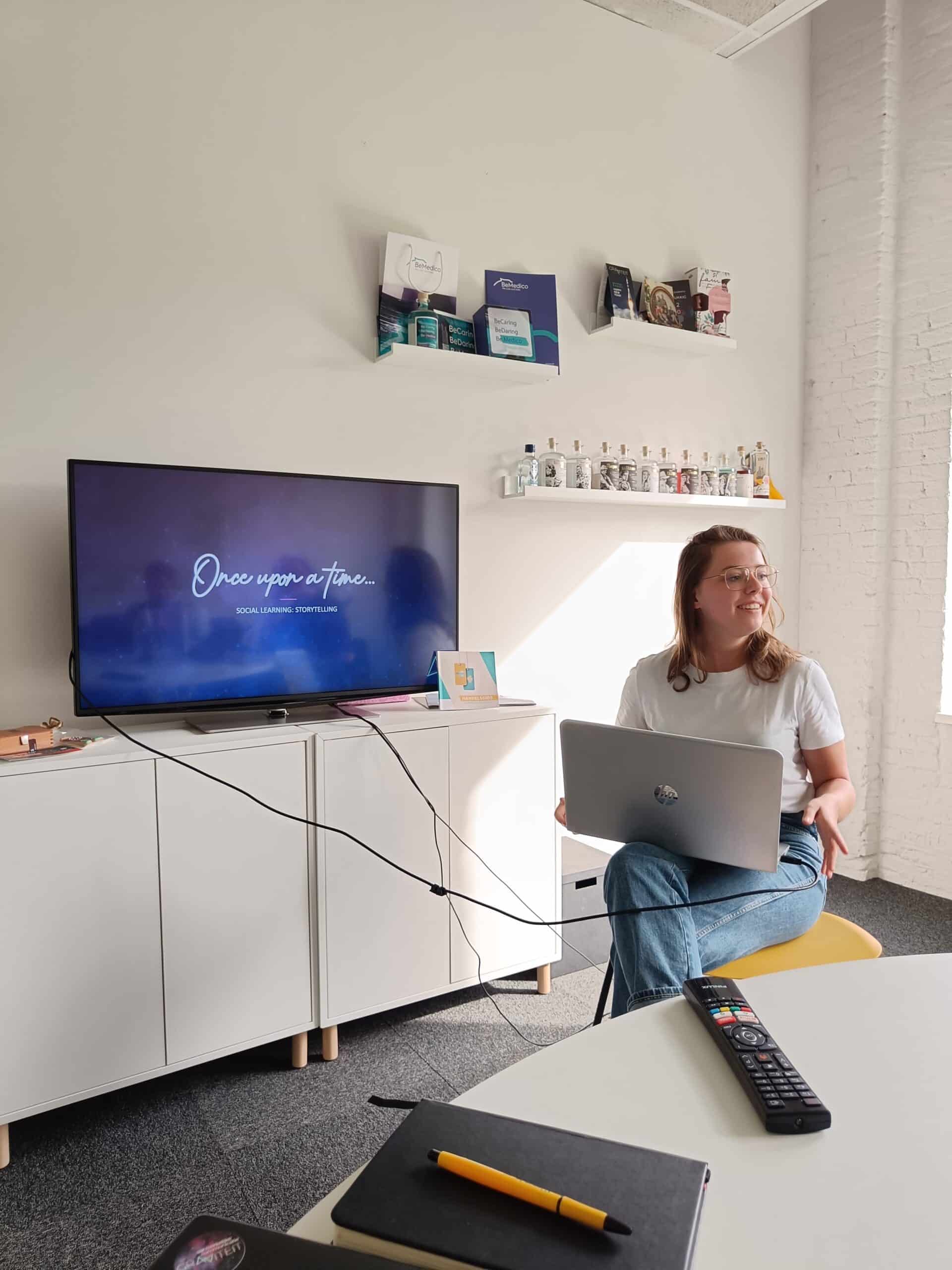 Stagiair Julie met een laptop geeft een presentatie in een vergaderruimte, op het scherm staat "Once upon a time... Social Learning & Storytelling".
