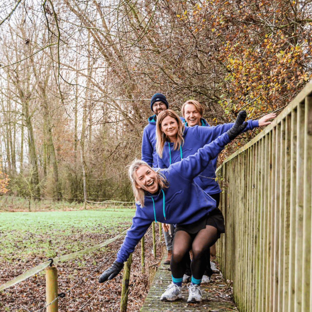 Het Graviteit-team in paarse BeMedico hoodies, lachend en poserend op een houten brug in een winters bos tijdens de eindejaar