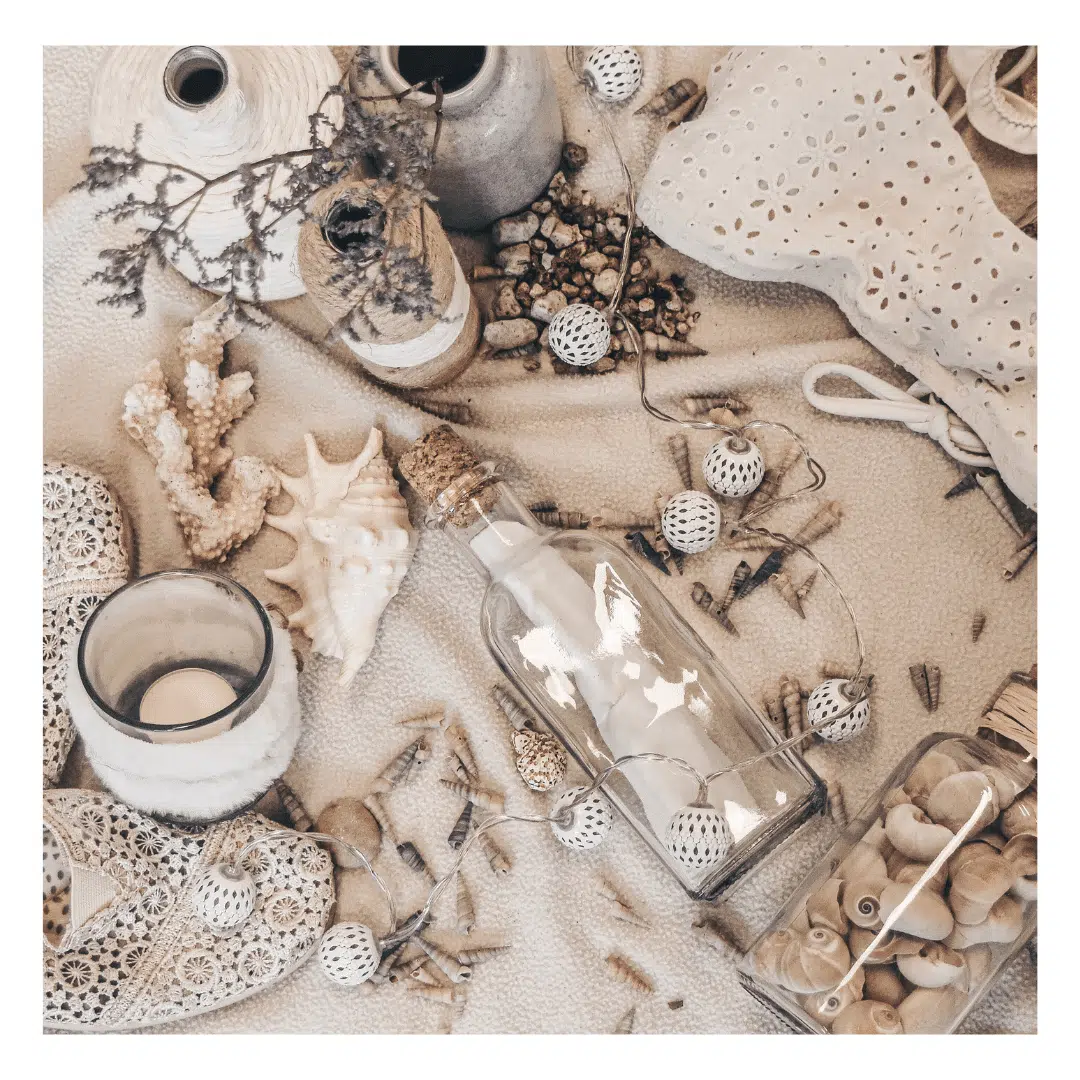 Een moodboard met strandthema op een lichte achtergrond. Te zien zijn schelpen, een glazen fles met een kurk, een kaars in een houder, een kanten kledingstuk, een gehaakte decoratie en gedroogde bloemen.