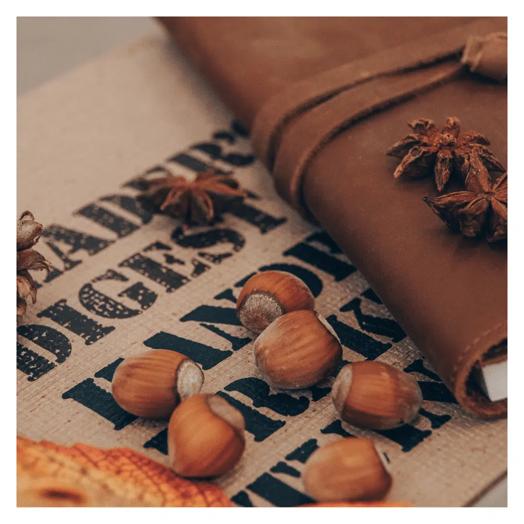 Een close-up van een moodboard met herfstthema. Te zien zijn hazelnoten, steranijs, een leren notitieboekje, en een doek met de tekst "READER'S DIGEST HANDYMAN'S BOOK".