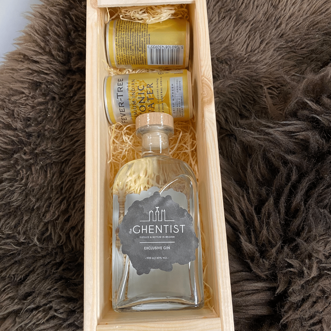 Een houten geschenkdoos met een fles exclusieve gin met het label "Ghentist," vergezeld van twee blikjes tonic water, op een harige achtergrond.