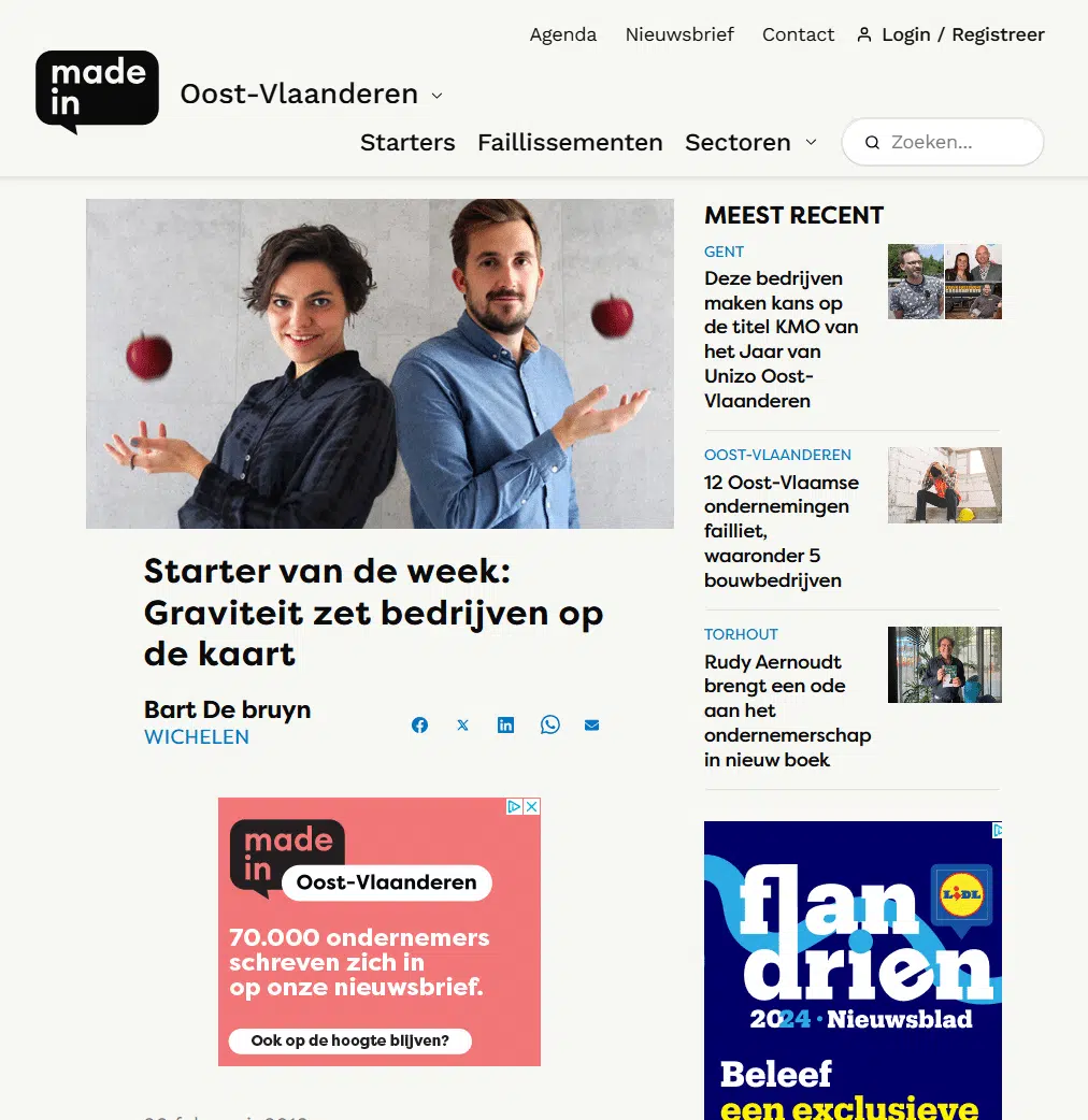 Graviteit Starter van de Week Beschrijving: Een nieuwsartikel over Graviteit als starter van de week. Frank Mertens en Ines Maroye staan naast elkaar en jongleren met appels. De titel van het artikel is "Starter van de week: Graviteit zet bedrijven op de kaart" geschreven door Bart De Bruyn. Aan de rechterkant van het artikel staan recent nieuws en advertenties. De website "Made in Oost-Vlaanderen" is zichtbaar met hun logo in de linkerbovenhoek.