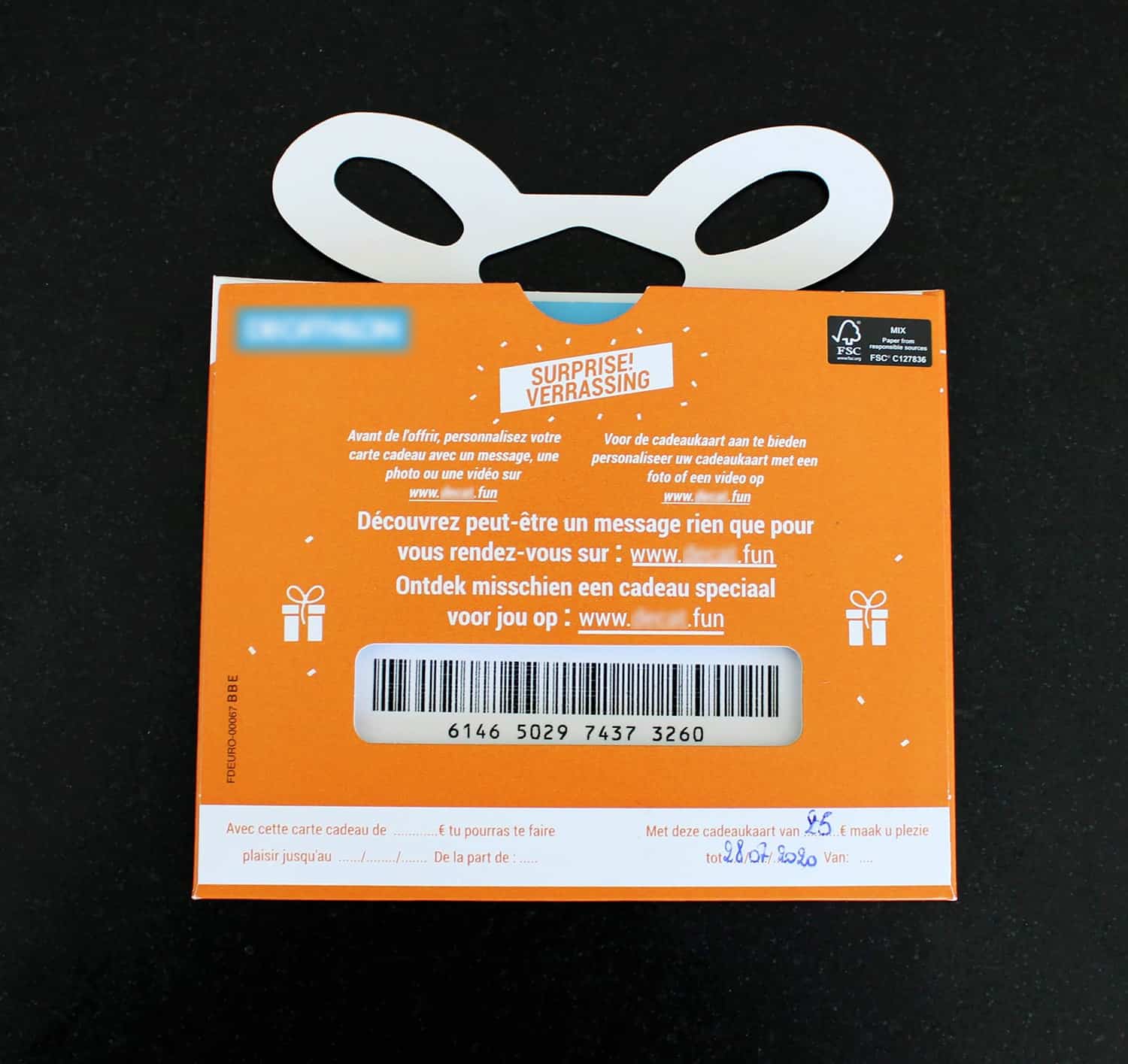 Achterkant van een oranje cadeaukaart verpakking met handvat en tekst in het Nederlands en Frans over het personaliseren van de kaart en een cadeau verrassing.