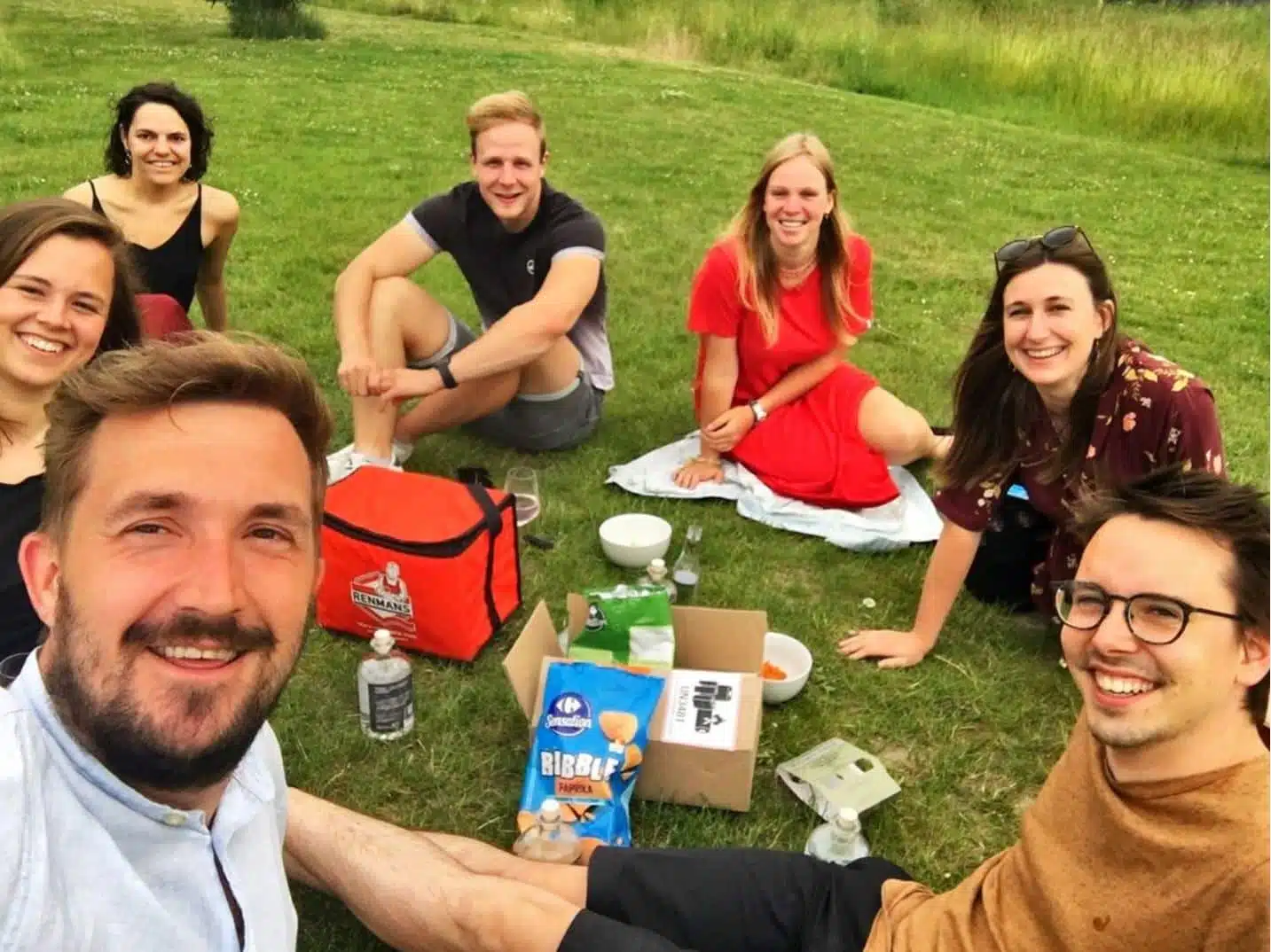 Het Graviteit team geniet van een picknick in het park. Ze zitten lachend op het gras, omringd door eten en drankjes, met een ontspannen en vrolijke sfeer.