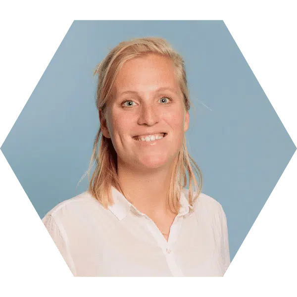 social media ondernemer congres Een hexagonale foto van een vrouw met blond haar, gekleed in een witte blouse, staand voor een lichtblauwe achtergrond. Ze glimlacht vriendelijk naar de camera.
