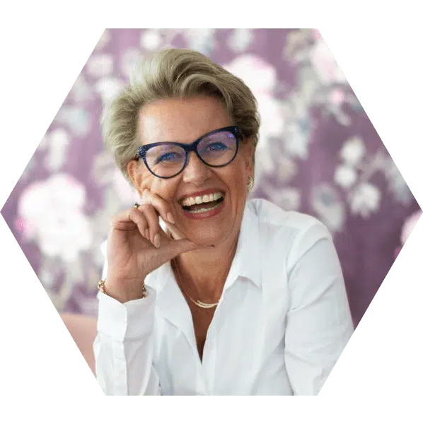 social media ondernemer congres Een hexagonale foto van een vrouw met kort, blond haar, een witte blouse en blauwe bril, lachend naar de camera, wat een vrolijke en open uitstraling creëert.