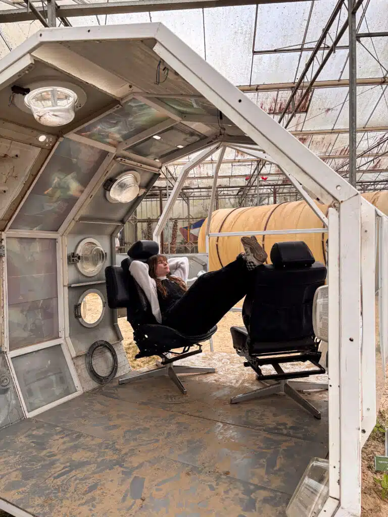Graviteit-teamlid Prisca ontspant in een futuristisch ruimteschip-installatie met zwarte stoelen in een industriële kas