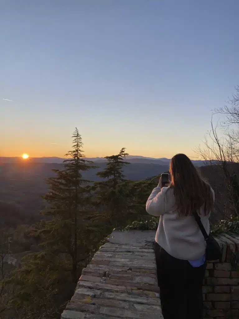 Prisca van Graviteit fotografeert een kleurrijke zonsondergang boven een berglandschap met haar smartphone, staand op een ste
