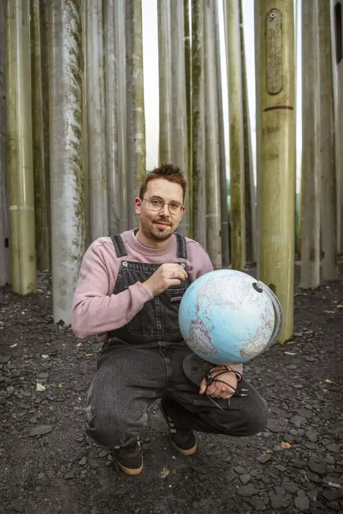 Graviteit teamlid in tuinbroek en roze trui houdt een wereldbol vast voor metalen pilaren, creatief bureau voor branding en c